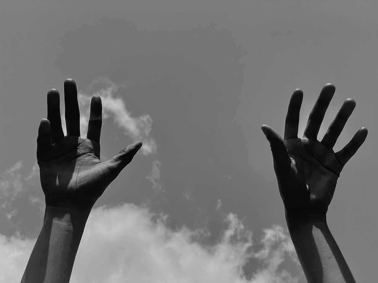 Black and white image of hands raised against a cloudy sky in Lagos.