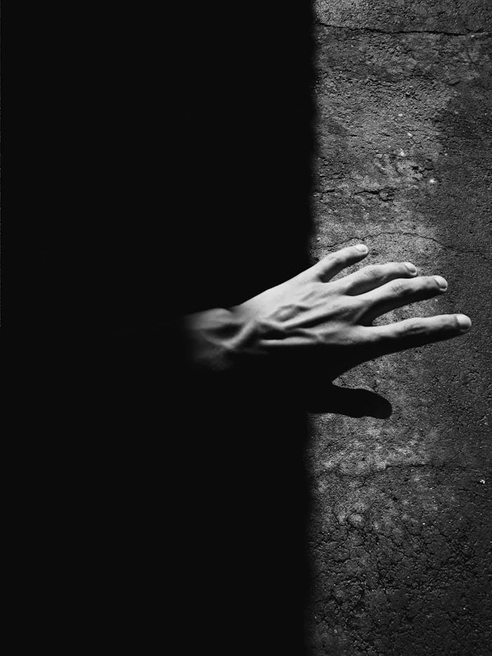Monochrome image of a hand reaching from darkness into light, high contrast.